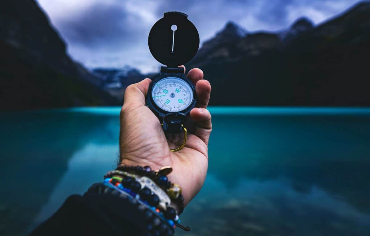 Someone holding a compass in front of a body of water to demonstrate finding your compass in life