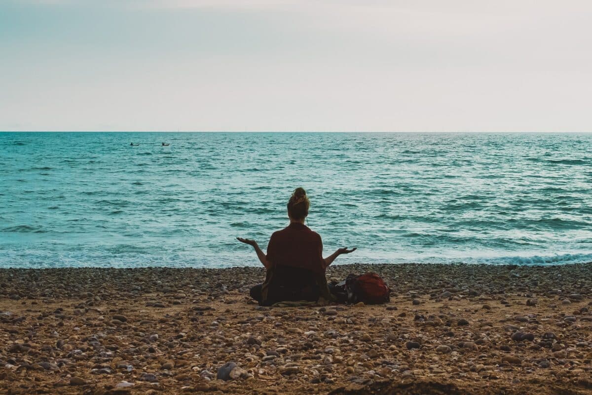 A person sitting on a beach in front of the water meditating. It shows the importance of mastering the art of 'yes and...'