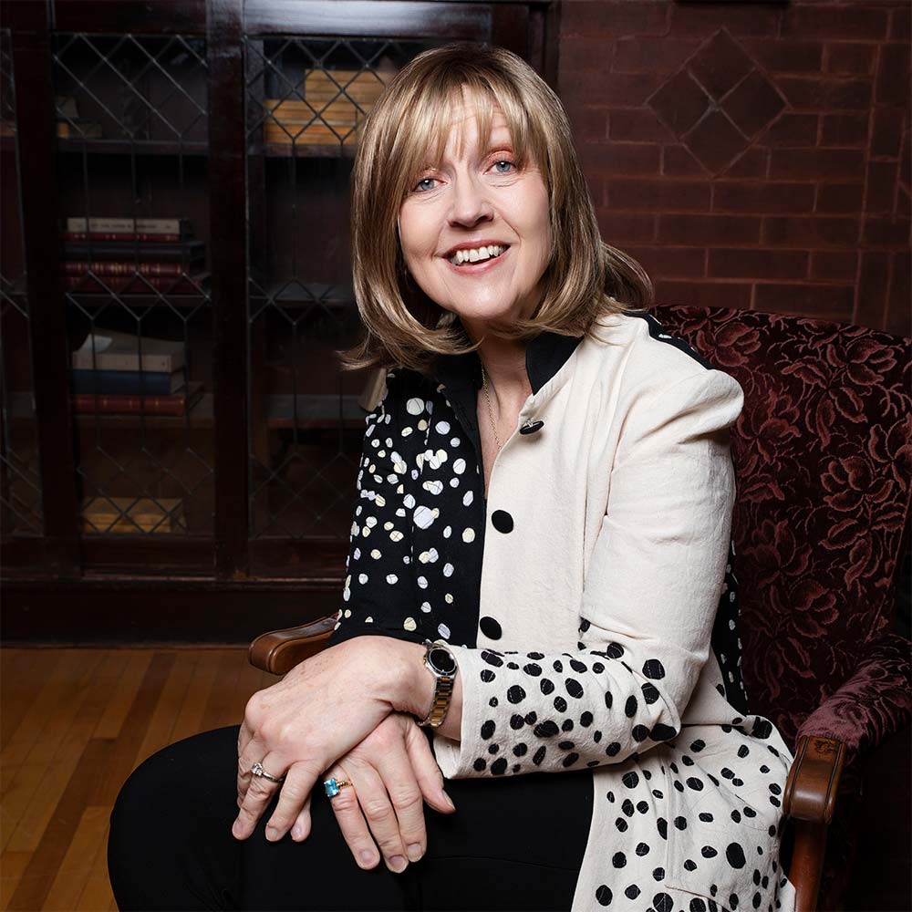Barb Stone sitting in a chair by an antique bookshelf