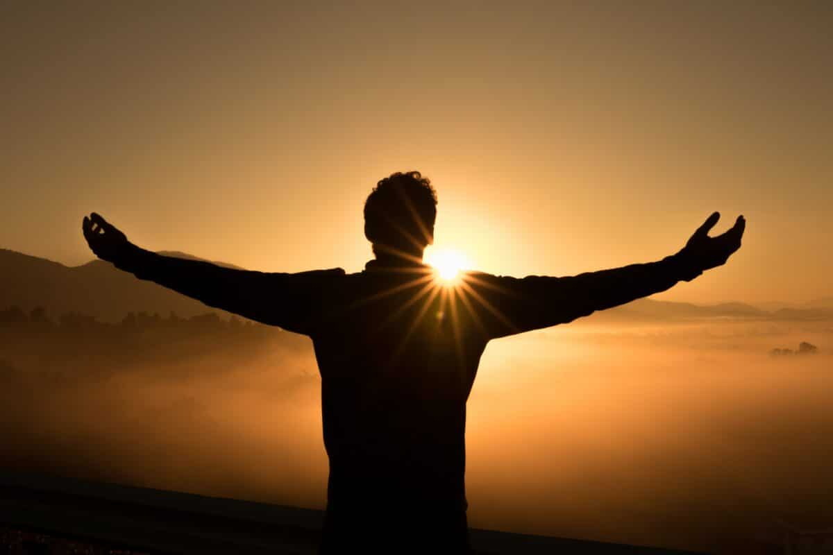 Someone standing in front of a sunrise with their arms outstretched