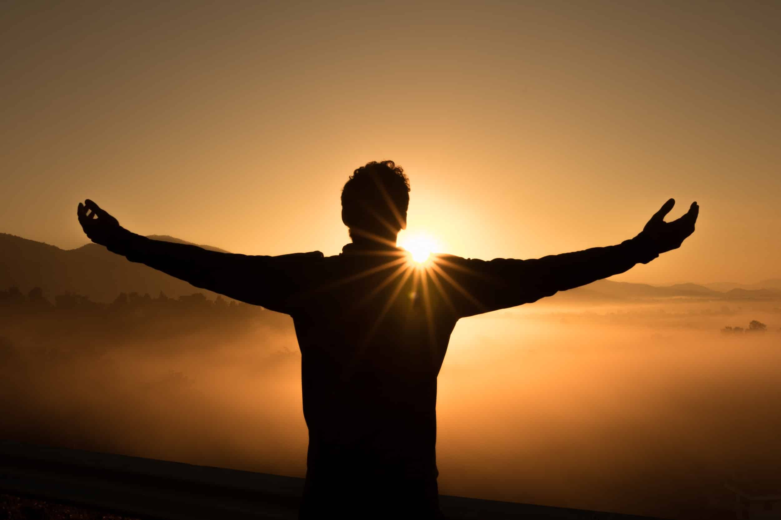 Someone standing in front of a sunrise with their arms outstretched